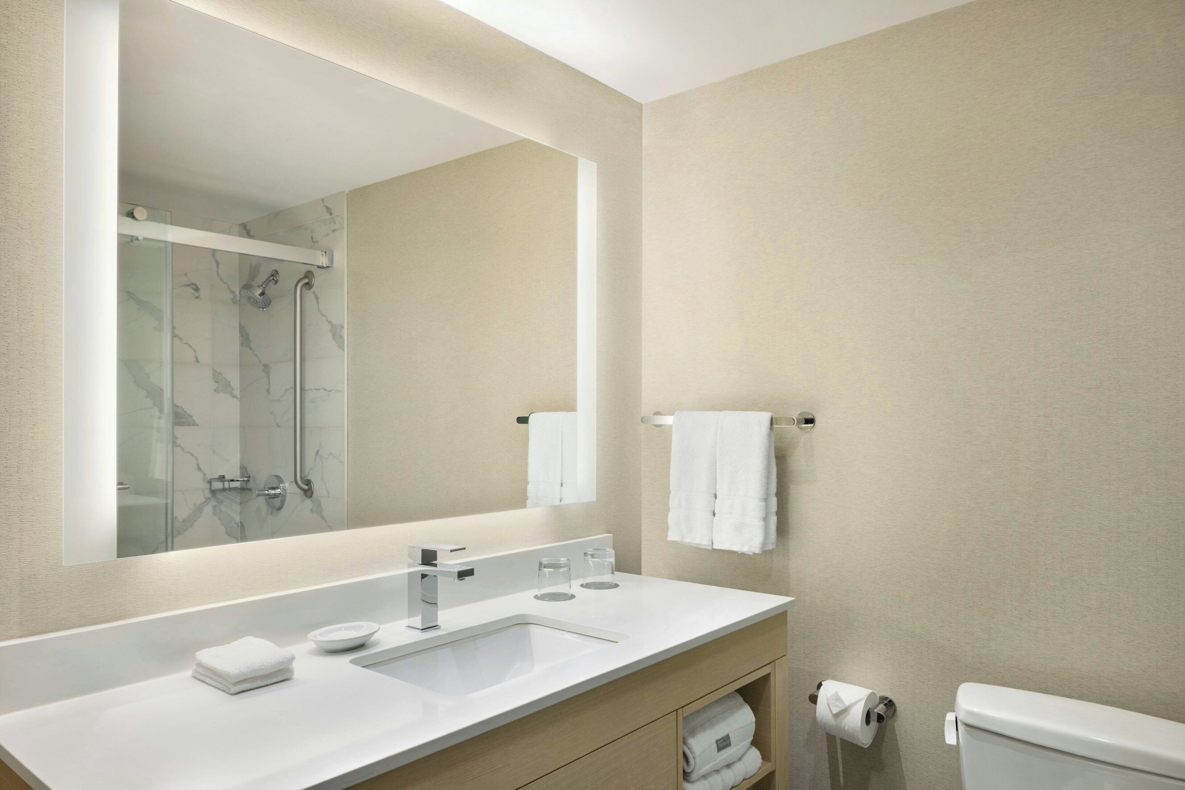 A modern bathroom with a large mirror, a white sink, a glass shower enclosure, and a toilet.
