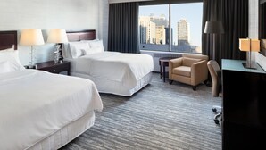 A hotel room with two beds, a desk, a chair, and a large window with a city view. - The Westin Edmonton (Edmonton)