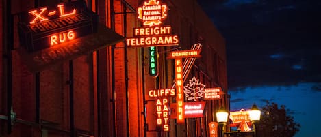 A building with multiple illuminated signs advertising various services such as furniture, rugs, and freight telegraphs.