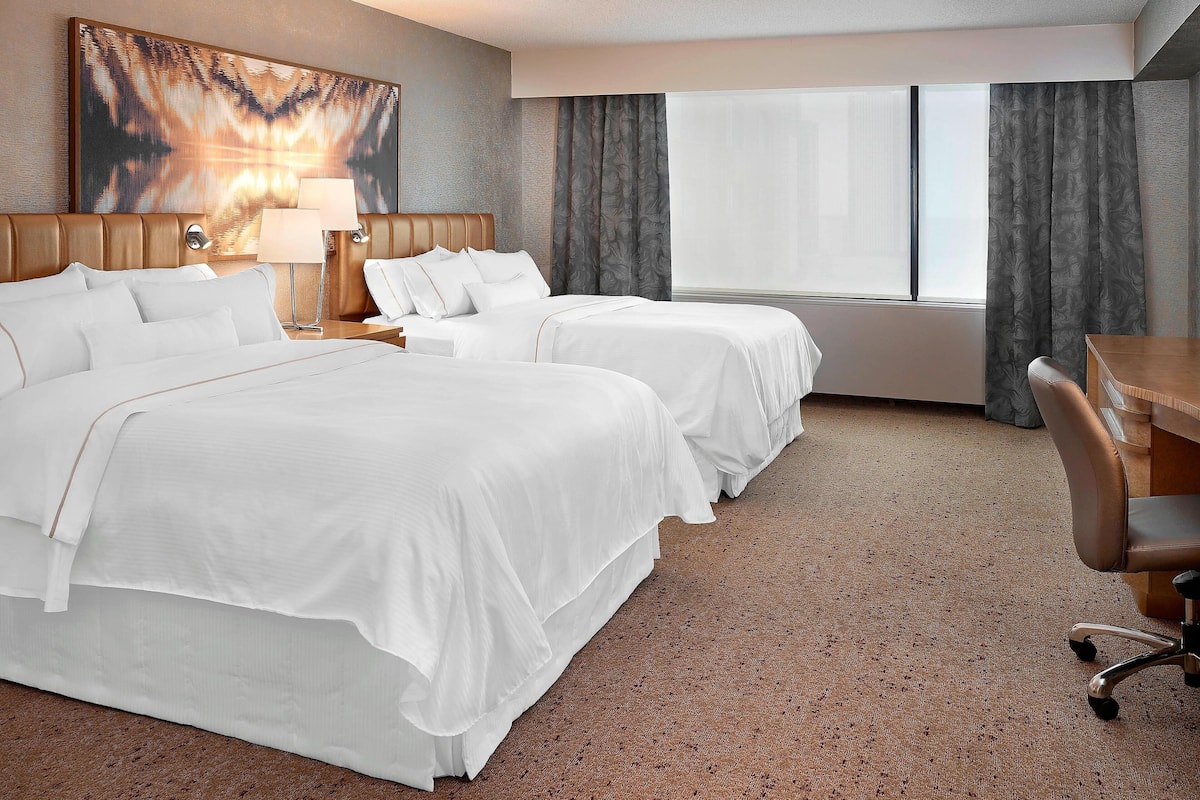 A hotel room with two beds, a desk, and a large window with curtains.