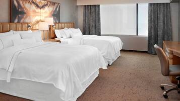 A hotel room with two beds, a desk, and a large window with curtains.