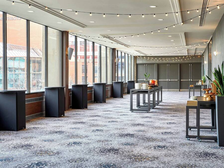 Une salle de conférence spacieuse et moderne, dotée de grandes fenêtres, d’un sol recouvert de moquette et d’une guirlande lumineuse.