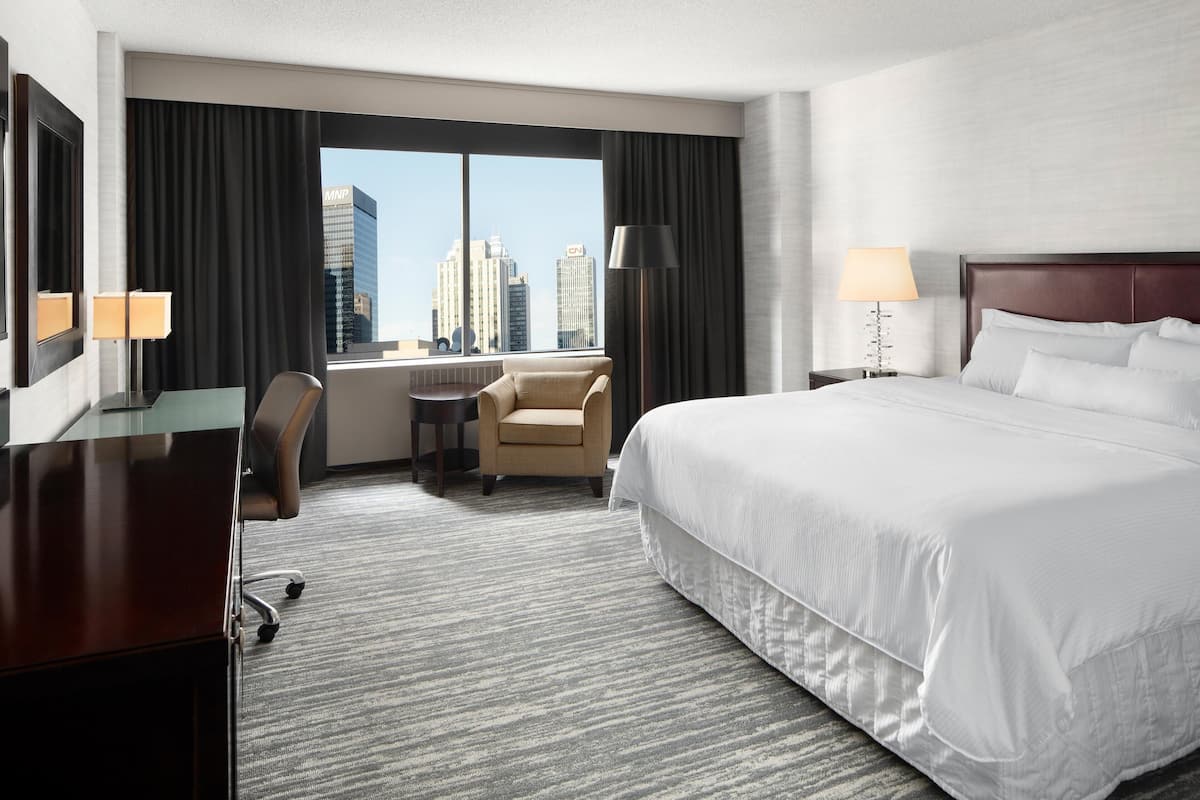 A hotel room with a large bed, a desk, a chair, and a view of the cityscape.