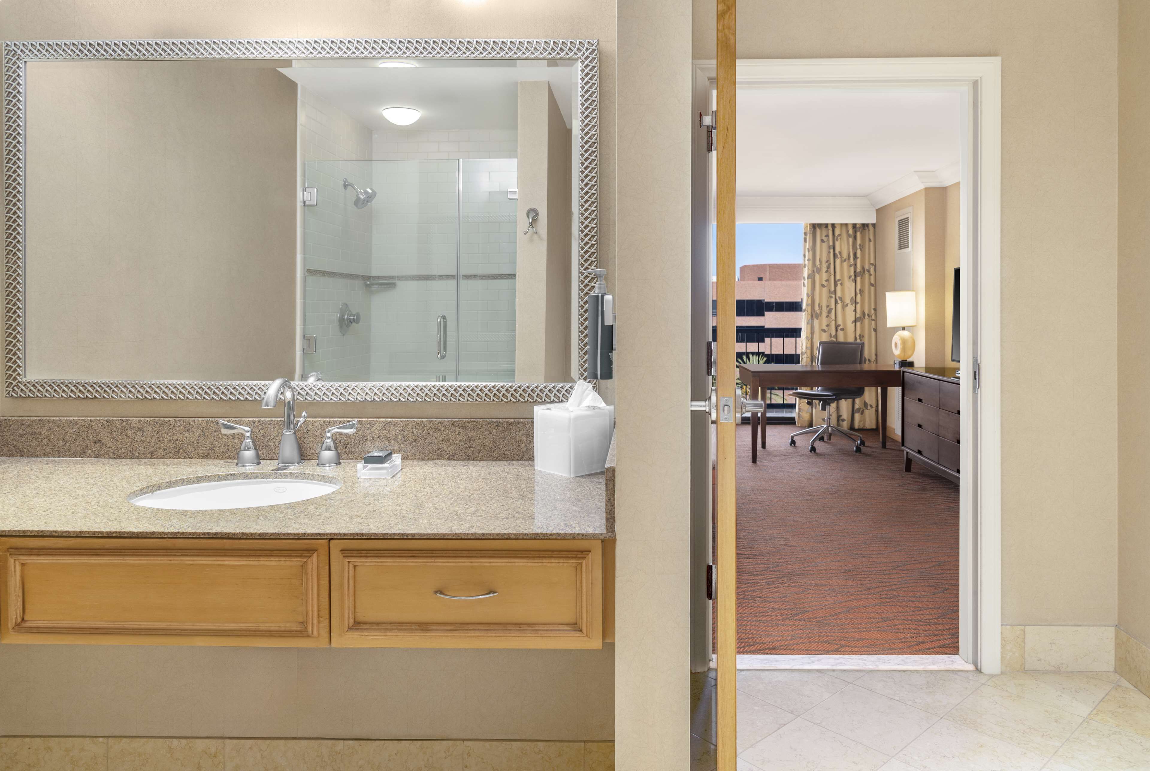 A hotel bathroom with a large mirror, two sinks, and a shower.