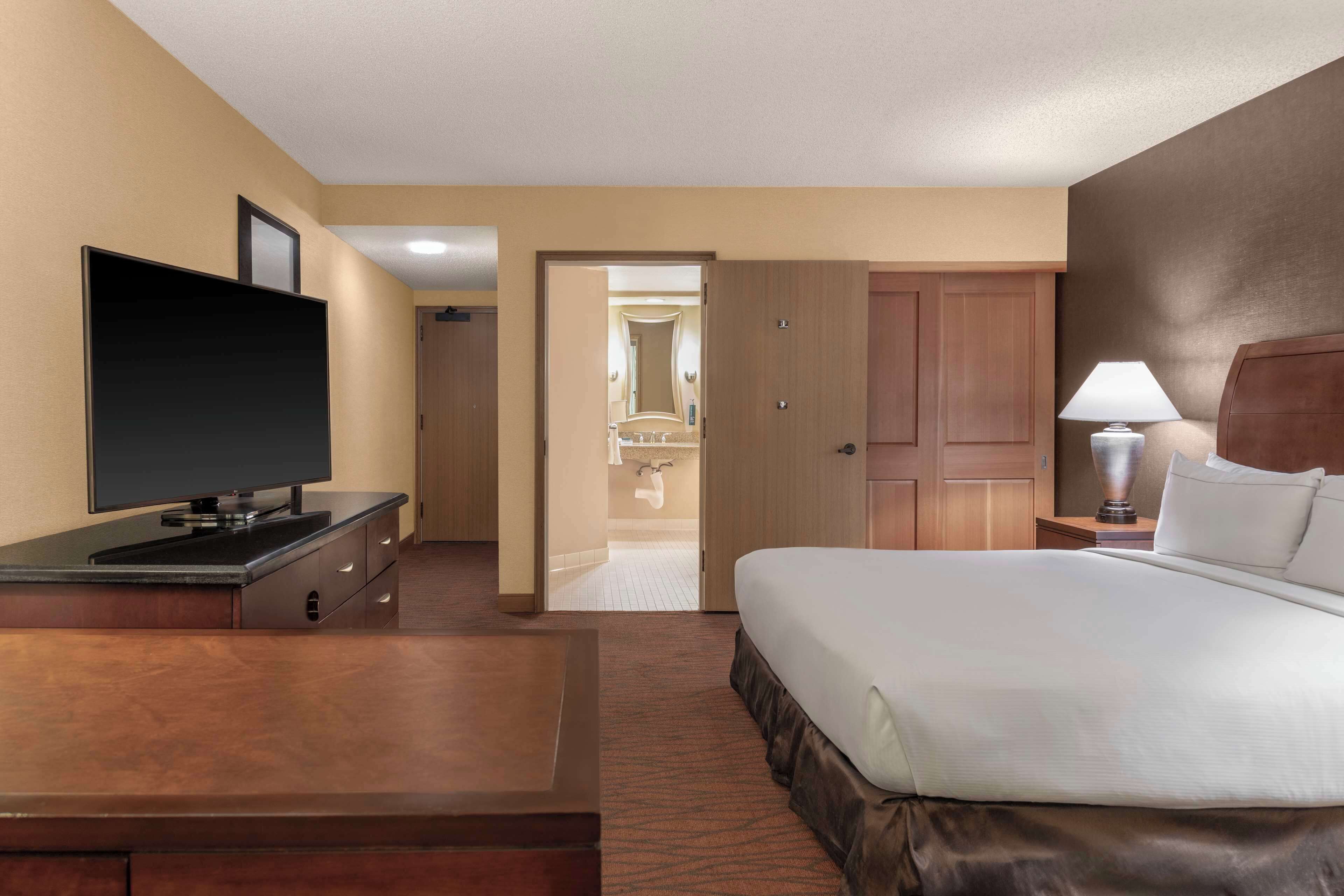 A hotel room with a bed, a TV, a desk, a lamp, and a bathroom visible through an open door.