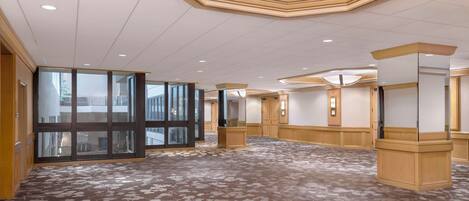 A spacious hotel lobby with a patterned carpet, large glass doors, and wooden columns.