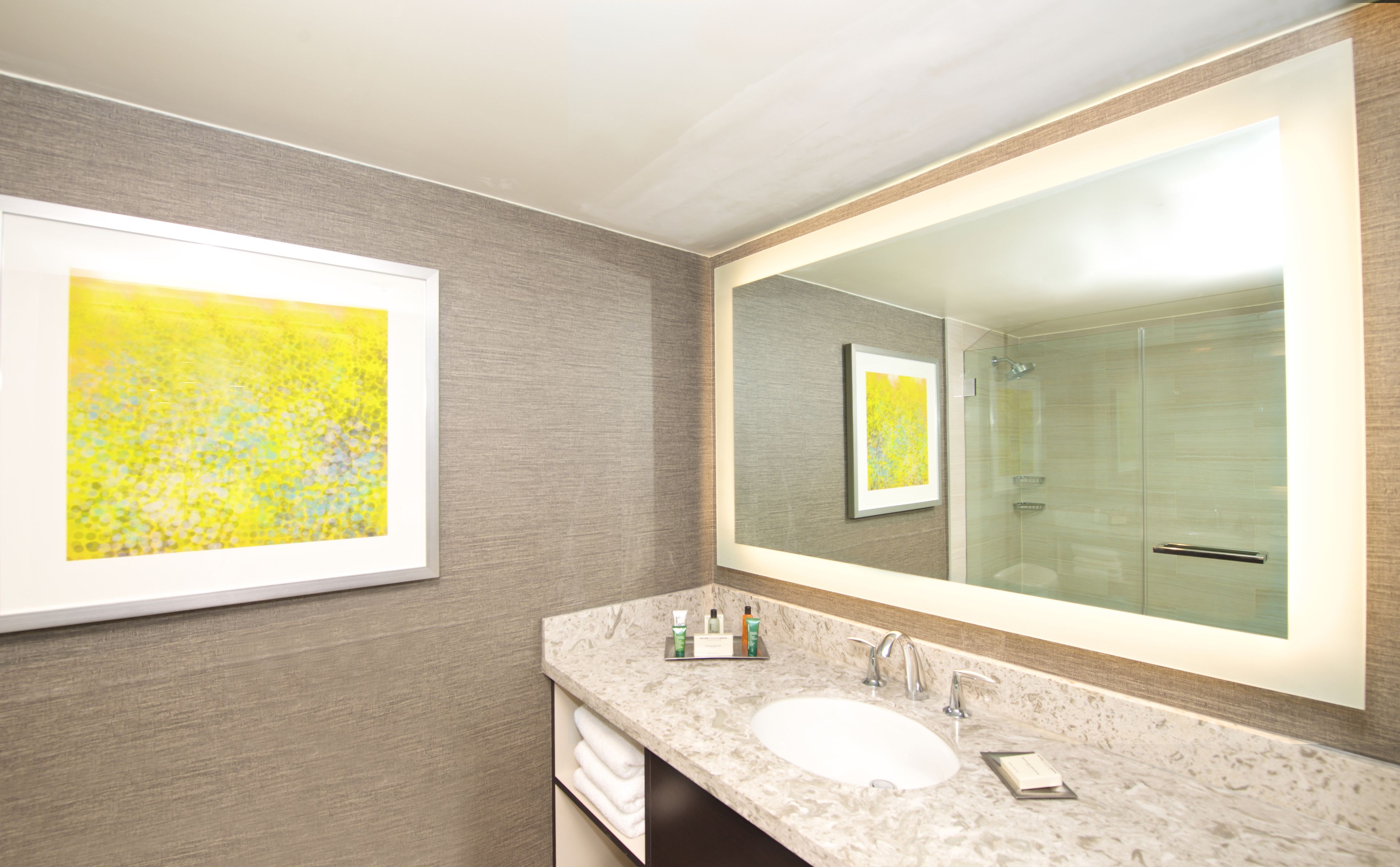 Un baño moderno con un espejo grande, un lavamanos de mármol y un cuadro abstracto enmarcado en la pared.