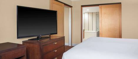 Habitación de hotel con una cama, un televisor sobre un aparador de madera, un espejo y una puerta corredera que da al baño.