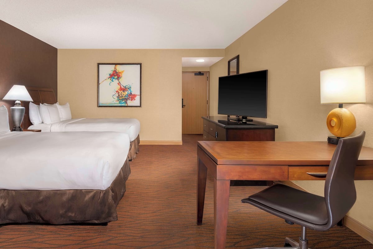 Quarto de hotel com uma cama, duas mesas de cabeceira, uma escrivaninha com cadeira, televisão e um quadro na parede.