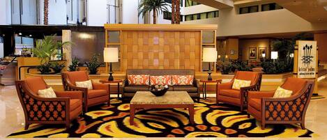 Un hall d’entrée doté d’un espace salon central comprenant des canapés et des fauteuils, un tapis à motifs et une cloison en bois ornée d’un motif tissé.
