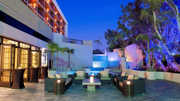 Un área lounge moderna al aire libre con asientos y una piscina, rodeada por un edificio con balcones y una cascada.