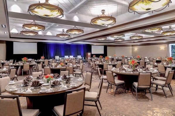 A large conference room with multiple round tables, each set with plates, cups, and cutlery.