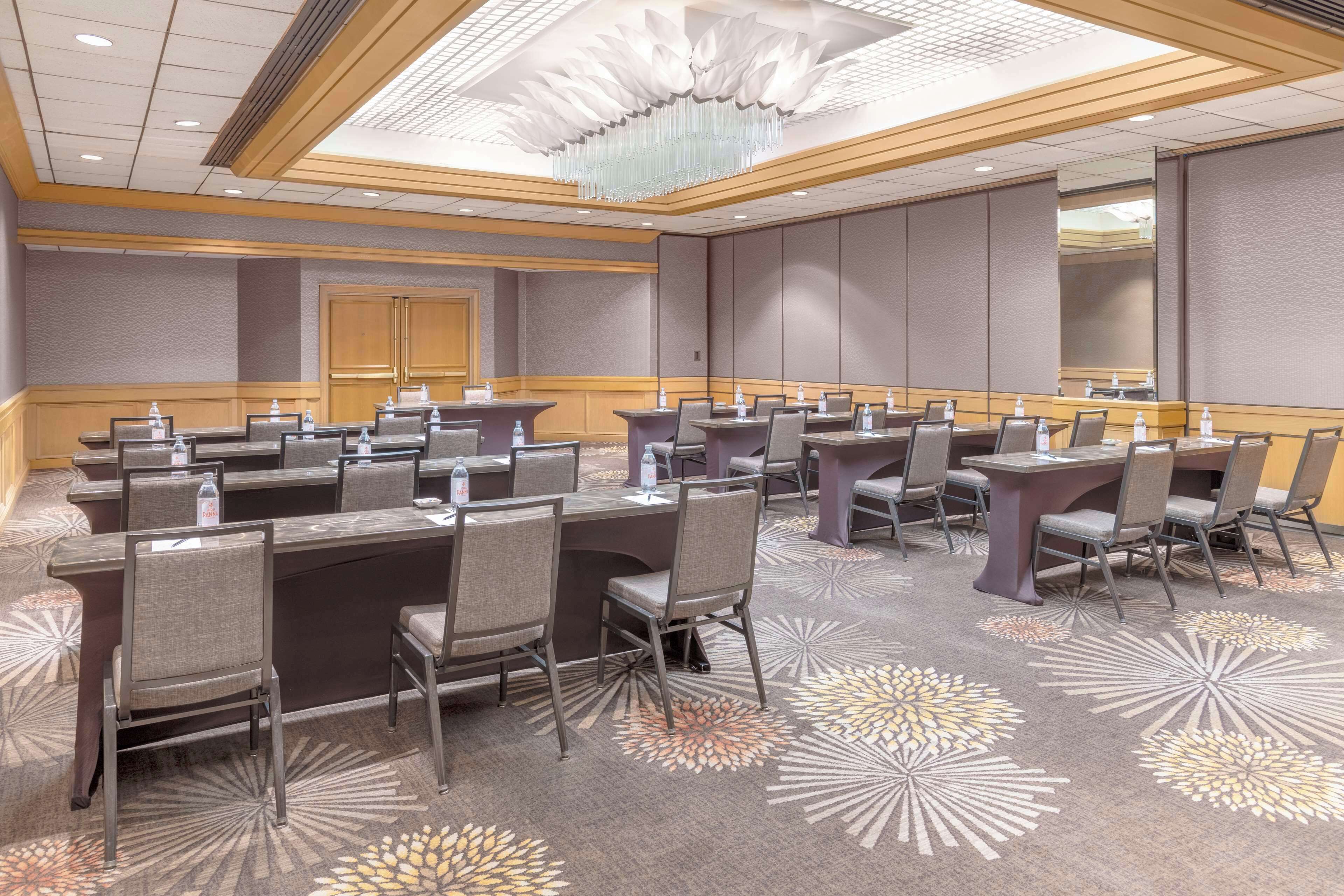 A conference room with multiple tables and chairs, equipped with water bottles, in a hotel setting.