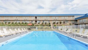 Una piscina con sillas de descanso y un edificio con varios balcones al fondo.