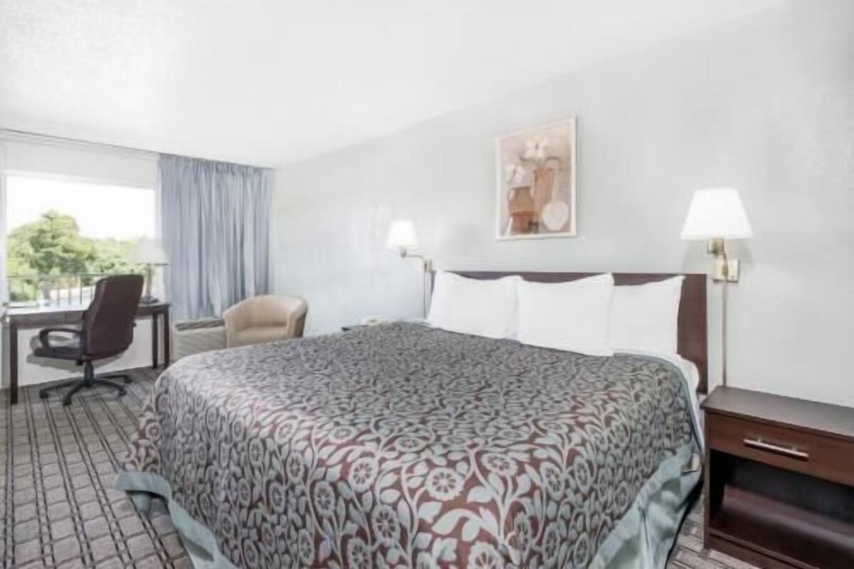 A hotel room with a large bed, a desk, a chair, and a window with a view.