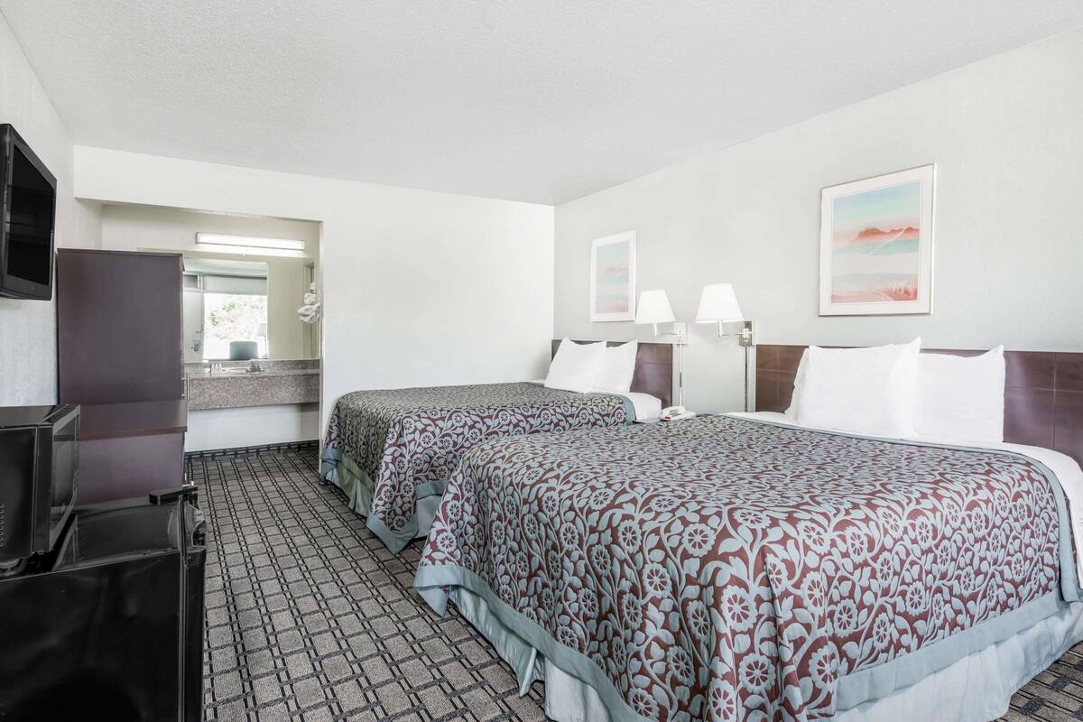 A hotel room with two beds, a TV, a desk, and a bathroom visible through an open door.