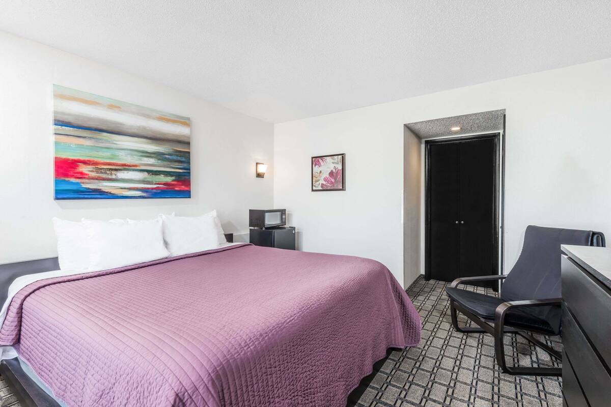 A hotel room with a bed, a desk, a chair, a microwave, and a door.