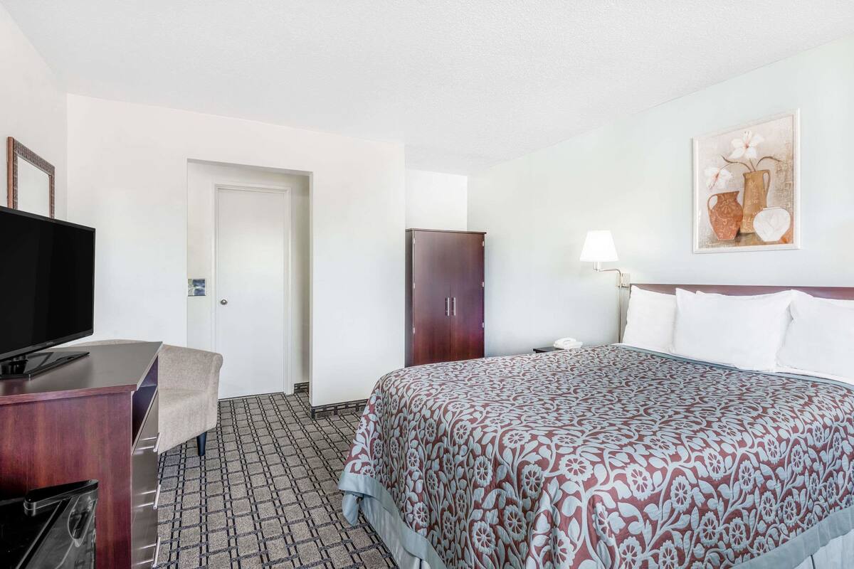 A hotel room with a bed, a television, a desk, a wardrobe, and a painting on the wall.