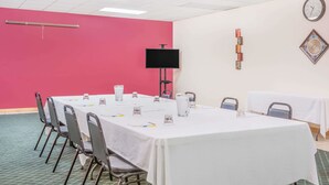 Un salón de conferencias con una mesa blanca, sillas, un televisor de pantalla plana y un reloj en la pared.