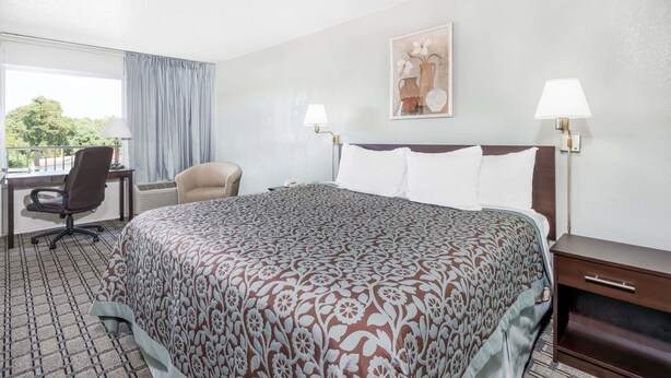 Una habitación de hotel con una cama grande, un escritorio, una silla y dos lámparas de noche.