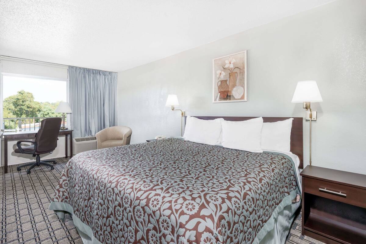 A hotel room with a large bed, a desk, a chair, and two bedside lamps.