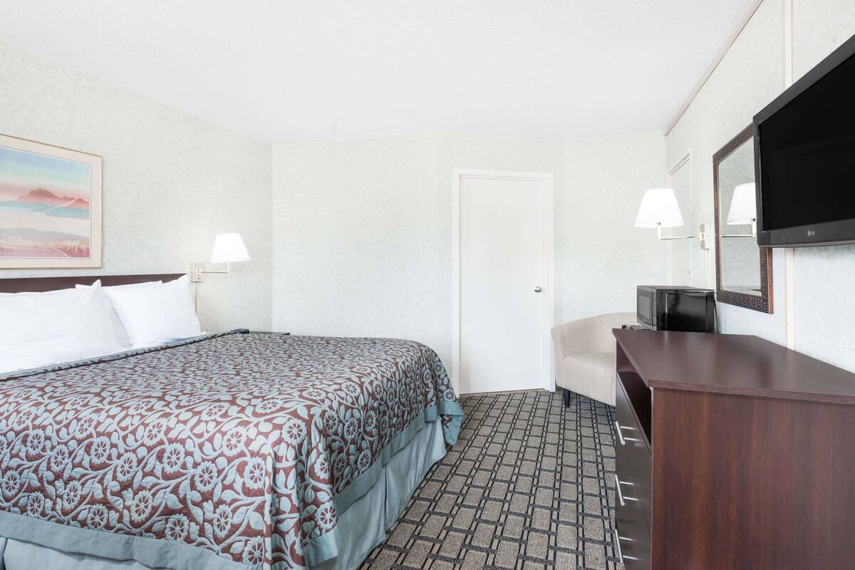 A hotel room with a bed, a desk, a television, and a door.