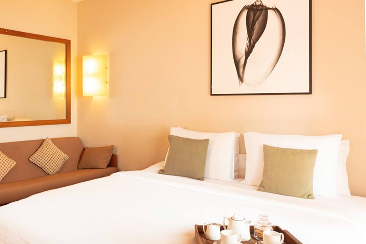 Une chambre d’hôtel avec un lit, une table d’appoint en bois sur laquelle est posé un service à thé, un canapé et une œuvre d’art encadrée au mur.