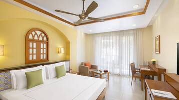 Una habitación de hotel con una cama grande, un ventilador de techo, una mesa de comedor con sillas y una ventana con cortinas.