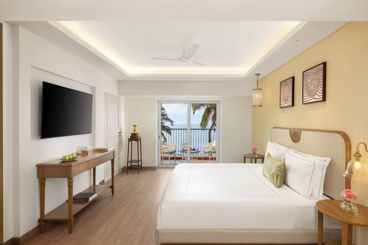 Une chambre d’hôtel avec un grand lit, un téléviseur fixé au mur, un bureau avec une lampe et une vue sur le balcon.