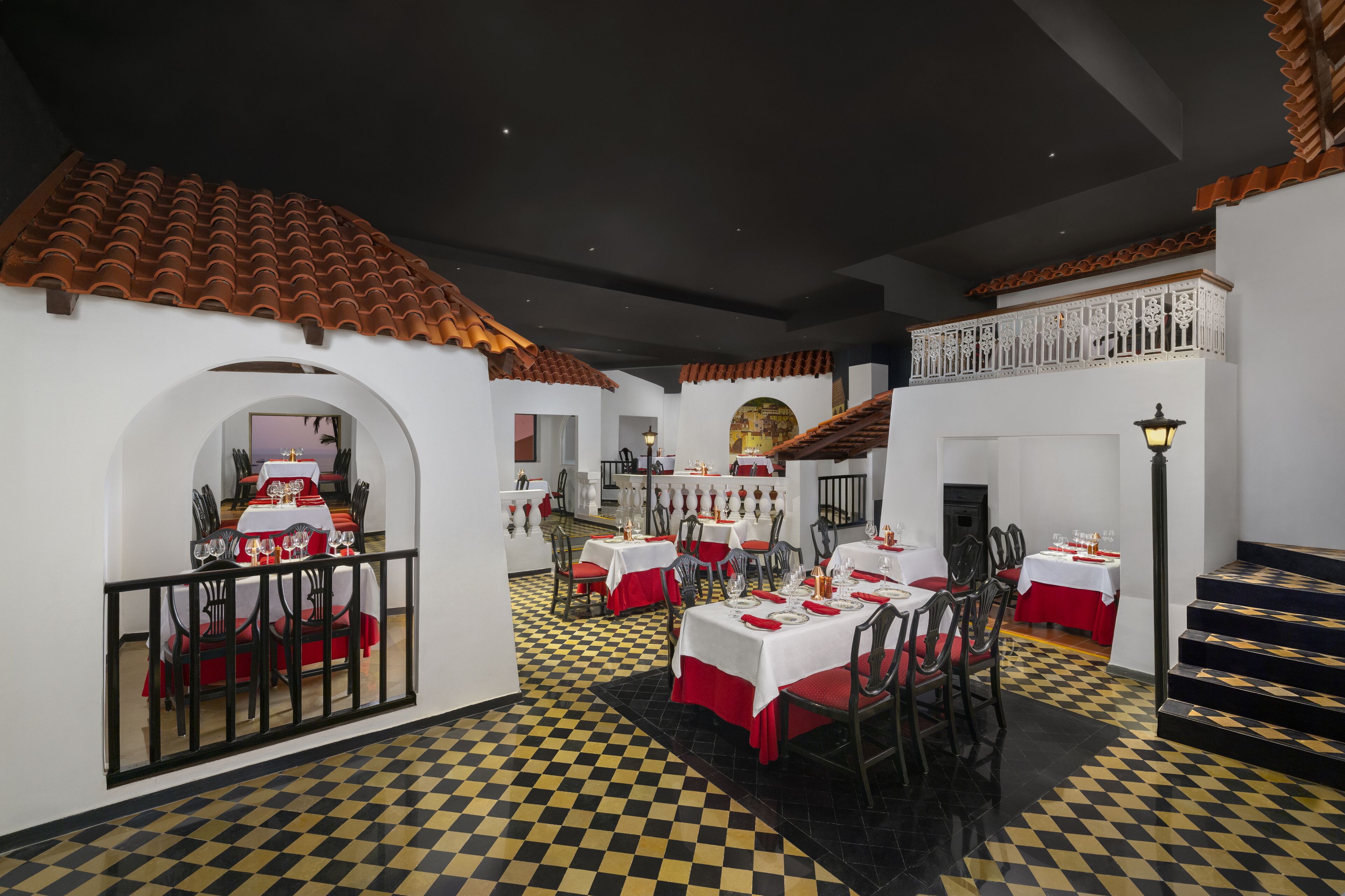 A restaurant with checkered flooring, white walls, and red accents. Tables are set with white tablecloths and red napkins.