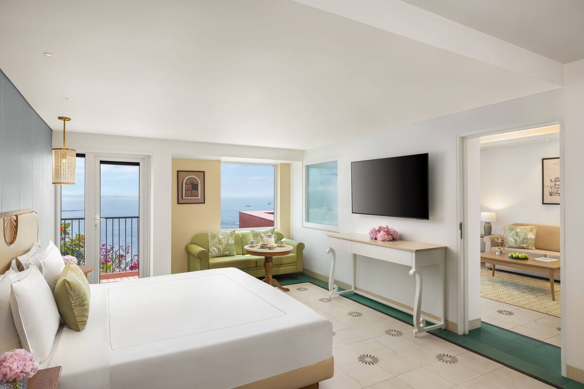 Une chambre d’hôtel avec un lit, un bureau, une télévision et un balcon donnant sur la mer.