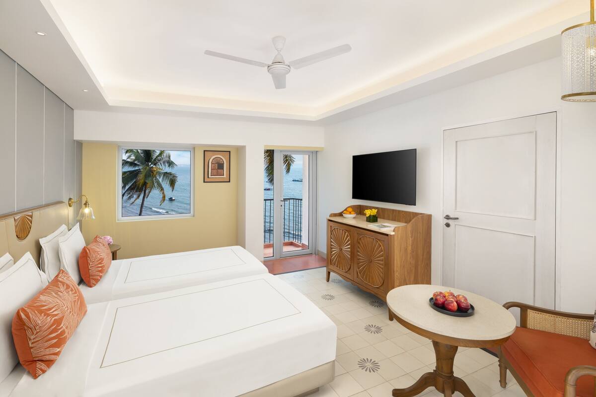 Une chambre d’hôtel avec deux lits, une télévision, une table à manger et une vue sur l’océan.