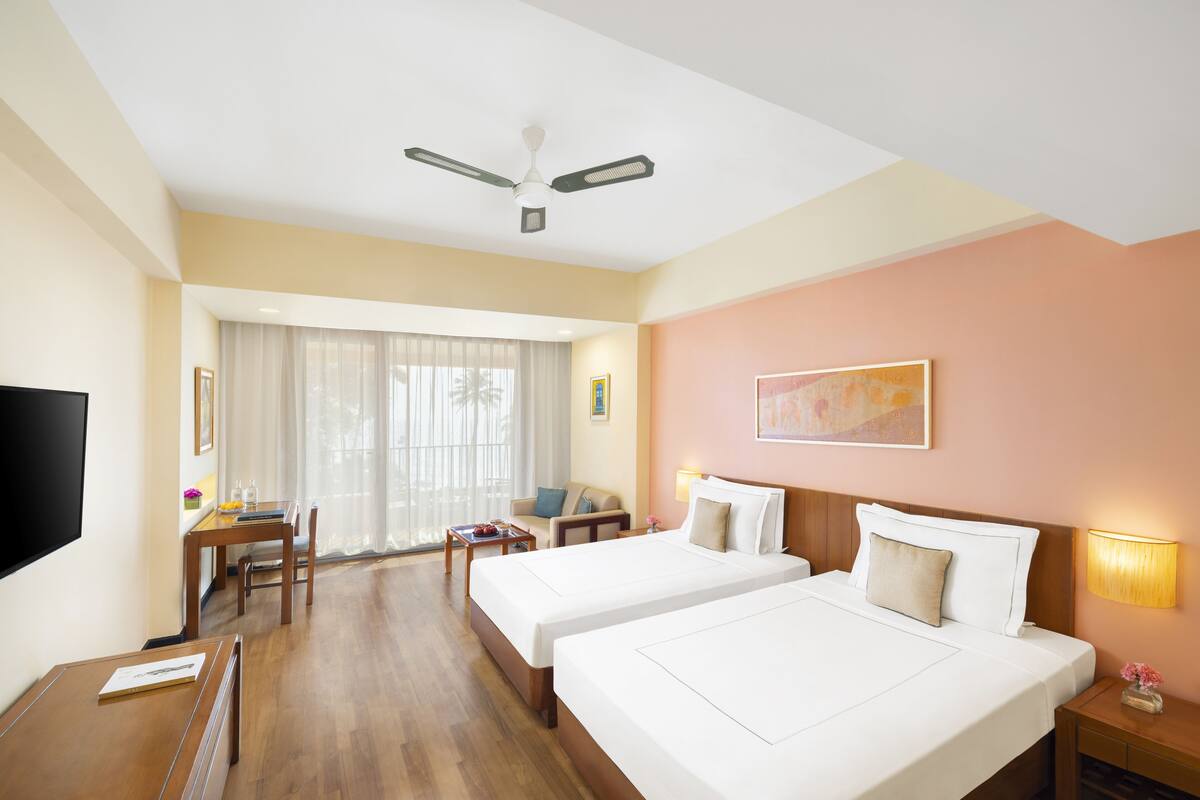 Une chambre d’hôtel avec deux lits, un bureau, une chaise, une télévision et un ventilateur de plafond.