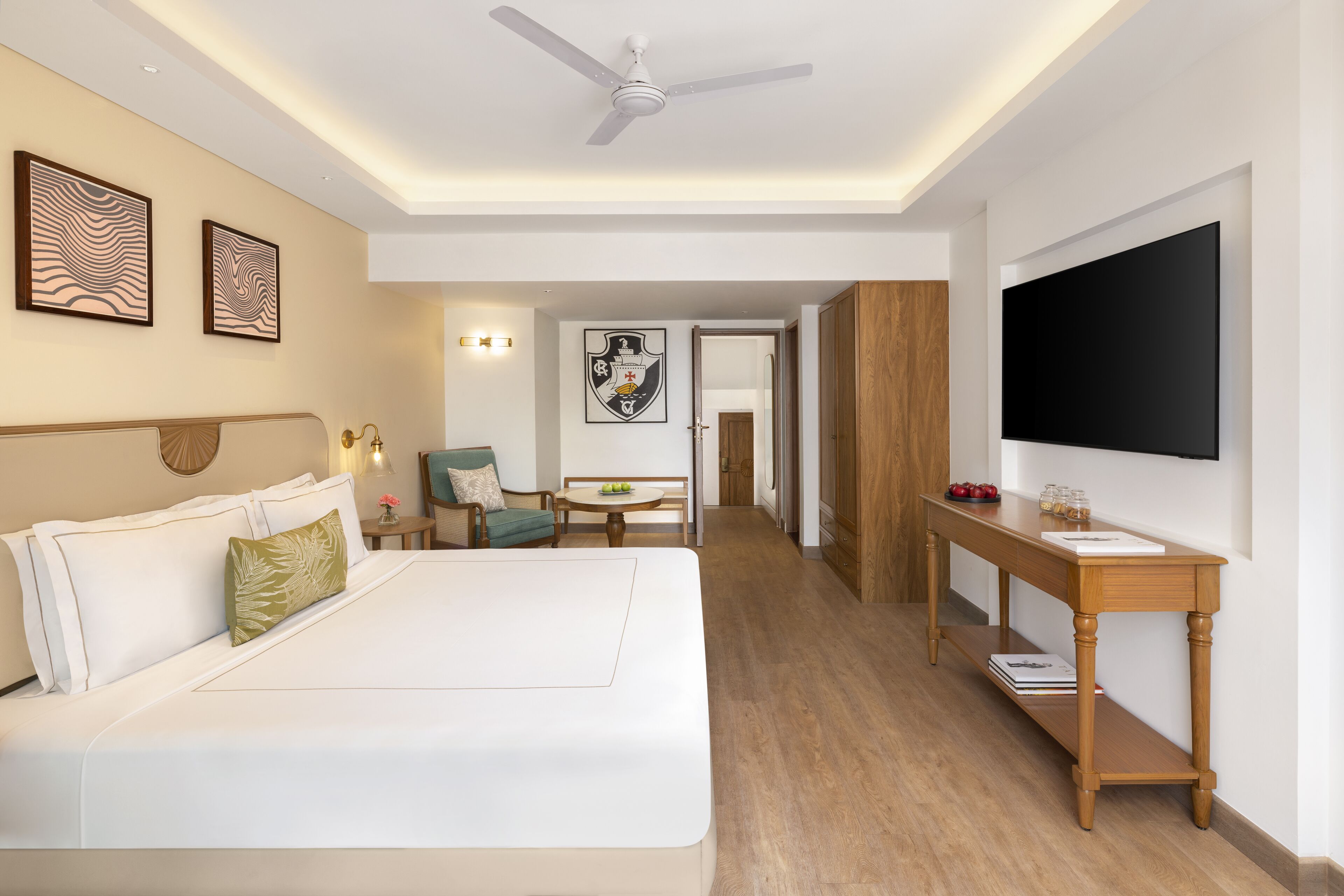 A hotel room with a large bed, a desk, a television, and a dining area.