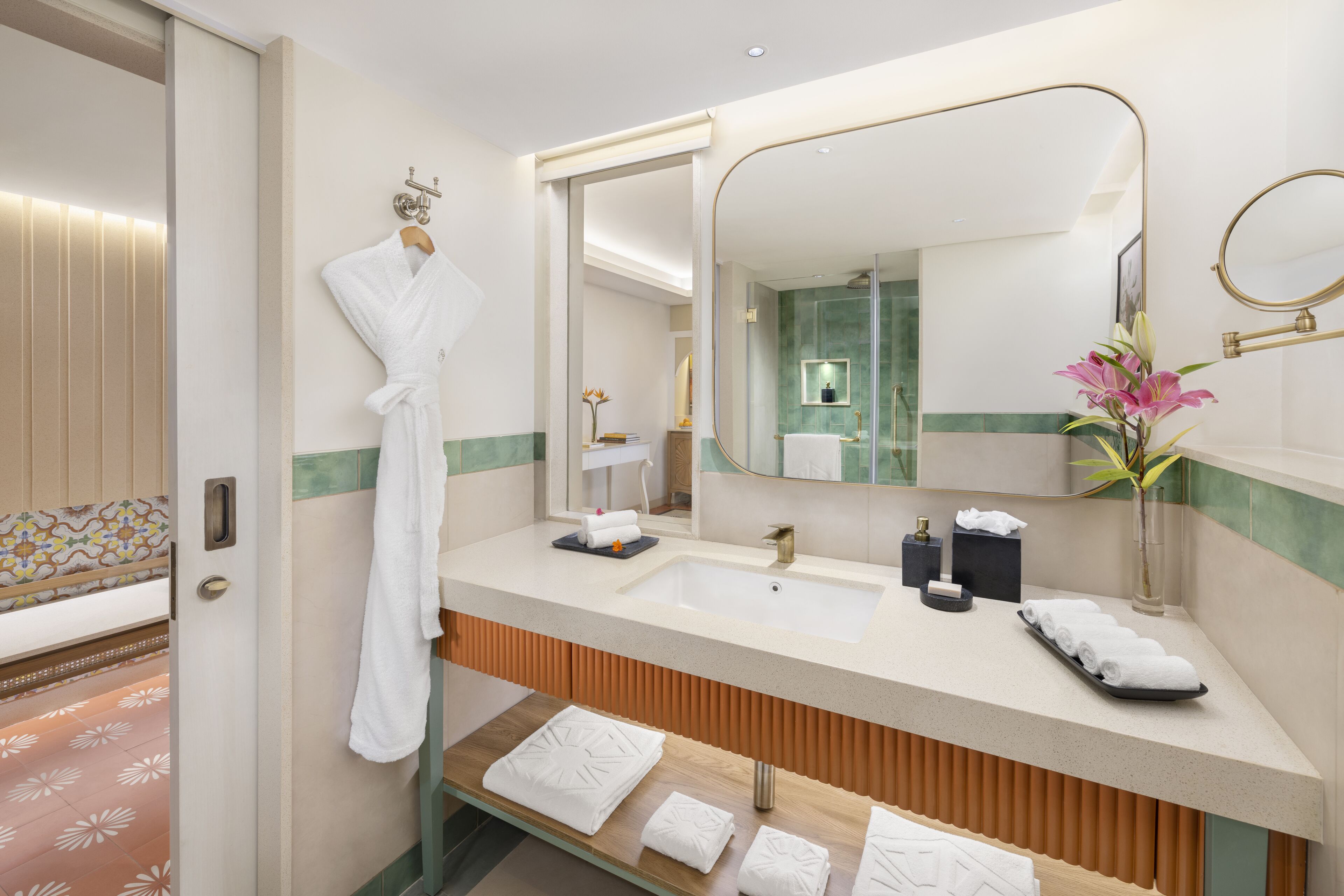 A modern bathroom with a large mirror, a sink, and a vanity. There is a robe hanging on the wall and a towel rack with towels.