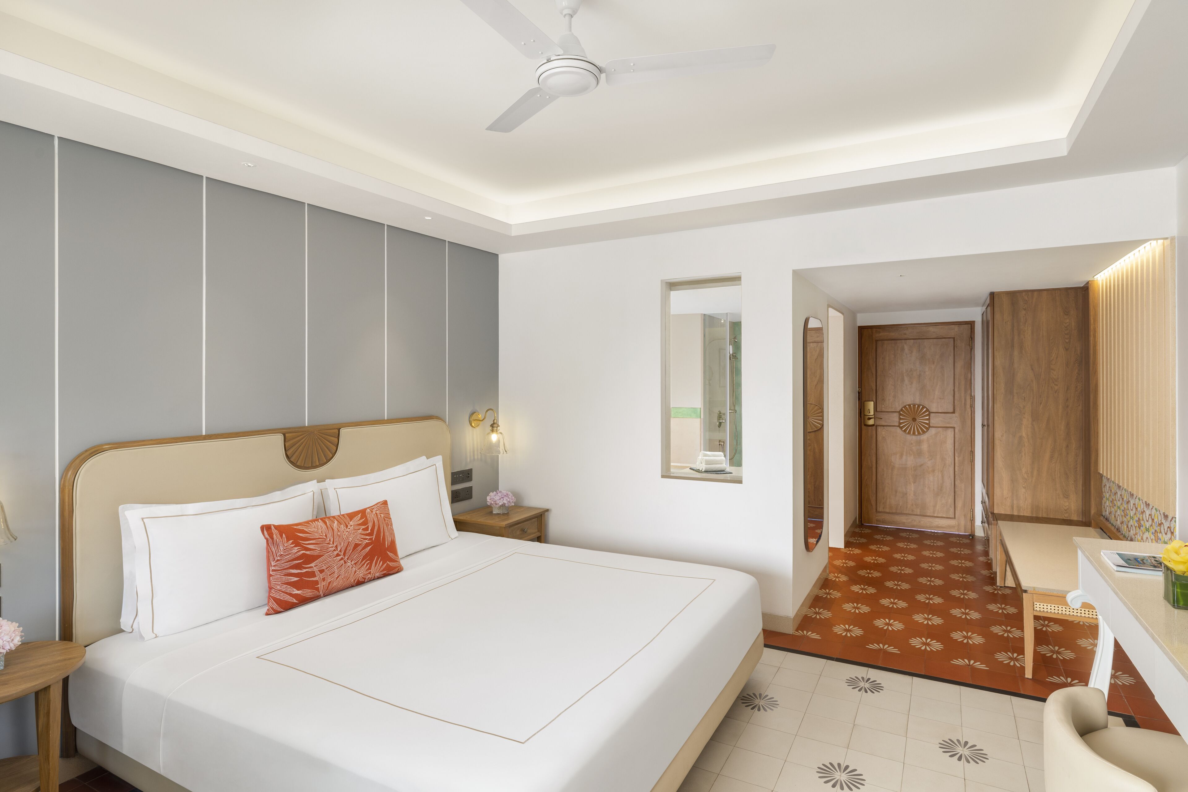 A hotel room with a large bed, a desk, a chair, a ceiling fan, and a door leading to a bathroom.