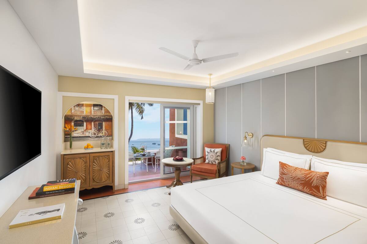 Une chambre d’hôtel équipée d’un lit, d’un bureau, d’une télévision, d’un ventilateur de plafond, offrant une vue sur l’océan et comprenant un balcon avec une table et des chaises.