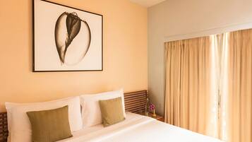 A hotel room with a large bed, a framed artwork on the wall, and a window with curtains.