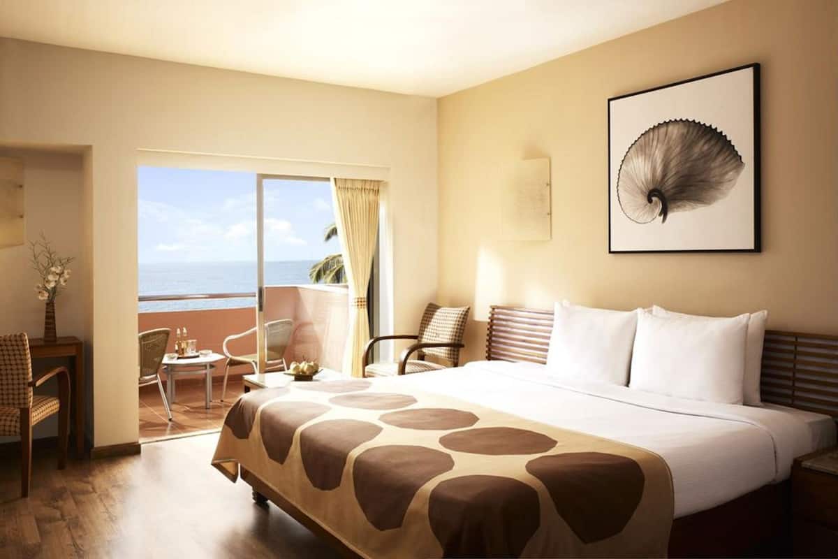Une chambre d’hôtel comprenant un lit, un bureau, des chaises, une vue sur l’océan et une grande œuvre d’art accrochée au mur.