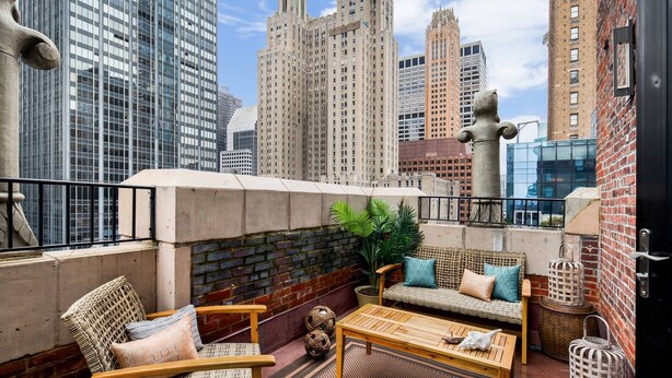 A rooftop terrace with wicker furniture, a potted plant, and decorative items against a cityscape backdrop.
