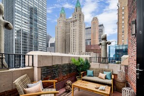Une terrasse sur le toit, aménagée avec des meubles en osier, un pot de fleurs et des objets décoratifs, le tout sur fond de paysage urbain.
