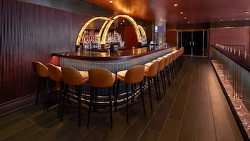 Zona de bar con una barra alargada, varios taburetes y una amplia selección de bebidas.