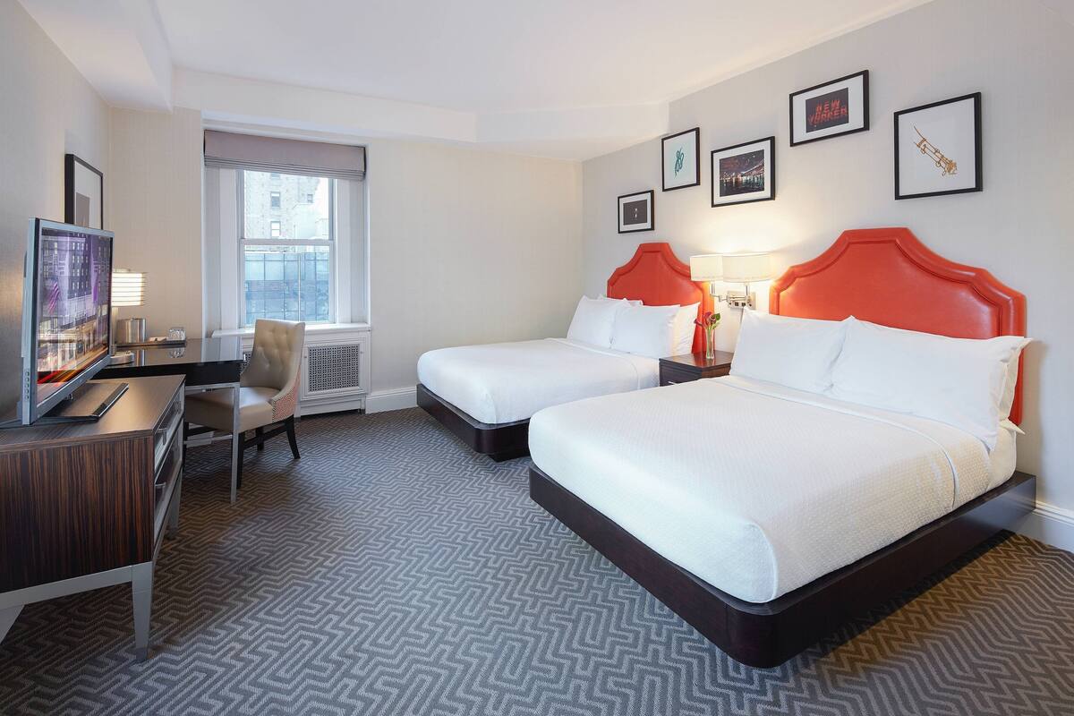 A hotel room with two beds, a desk, a chair, a TV, and framed pictures on the wall.