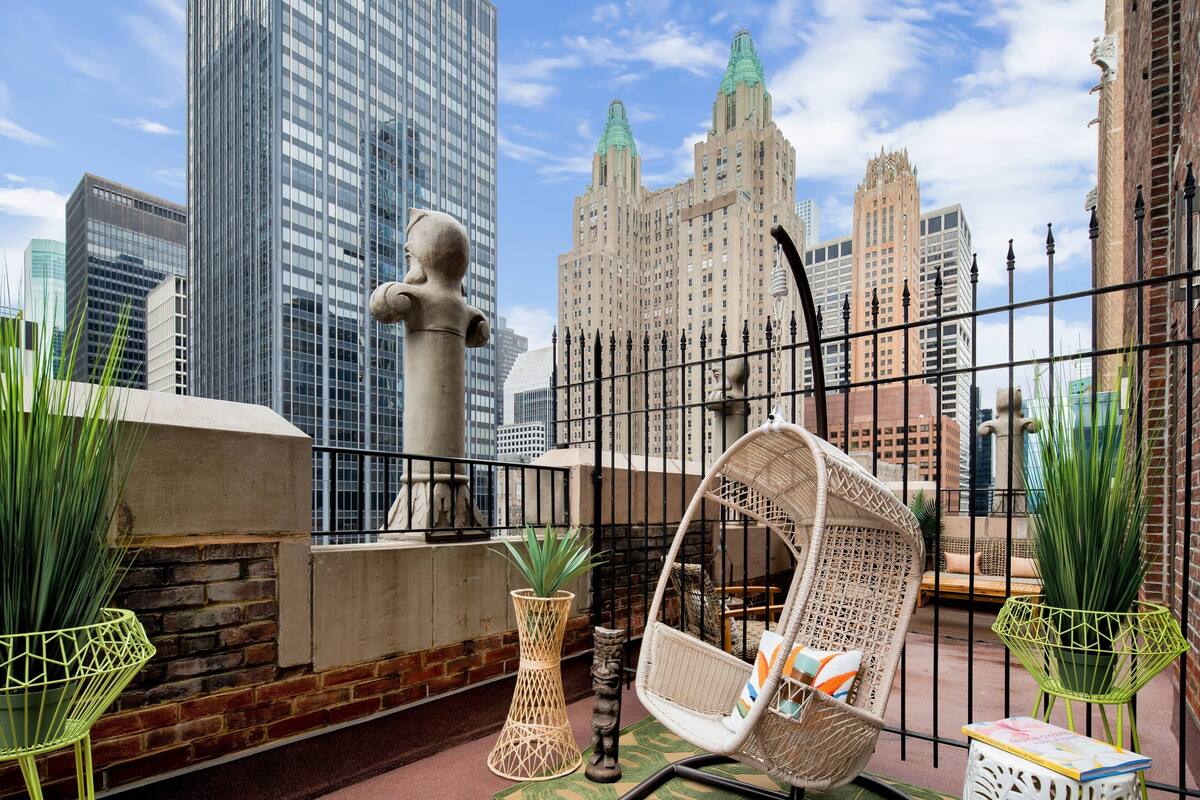 A rooftop terrace with a wrought iron fence, a white wicker chair, and potted plants.