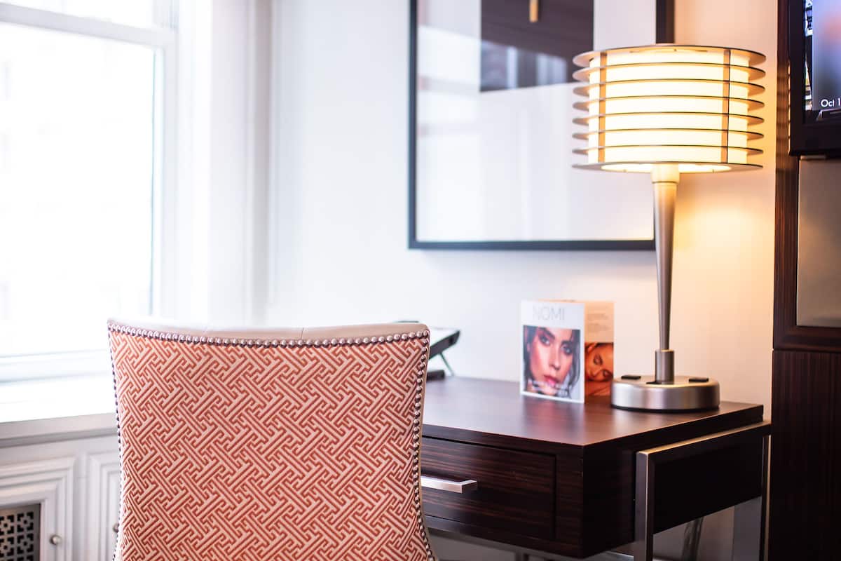 Habitación de hotel con un sillón estampado, un escritorio con lámpara y un cuadro en la pared.
