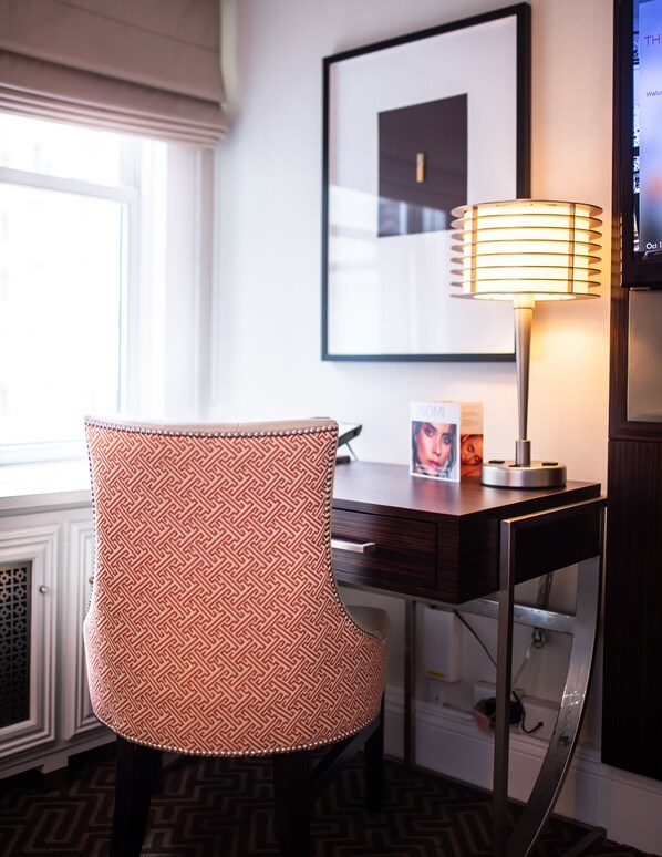 Une chambre d’hôtel avec un fauteuil à motifs, un bureau avec une lampe et un tableau encadré au mur.