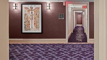 Un couloir d’hôtel avec un tapis à motifs, une œuvre d’art encadrée au mur et des panneaux de signalisation.