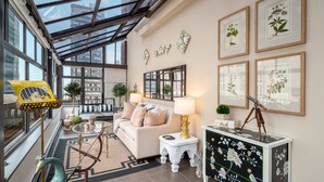 A modern living room with a glass ceiling, a sofa, a coffee table, and framed botanical prints on the wall.