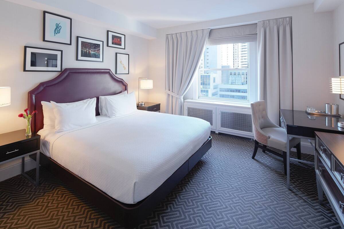 A hotel room with a large bed, a desk, a chair, and a window with curtains.