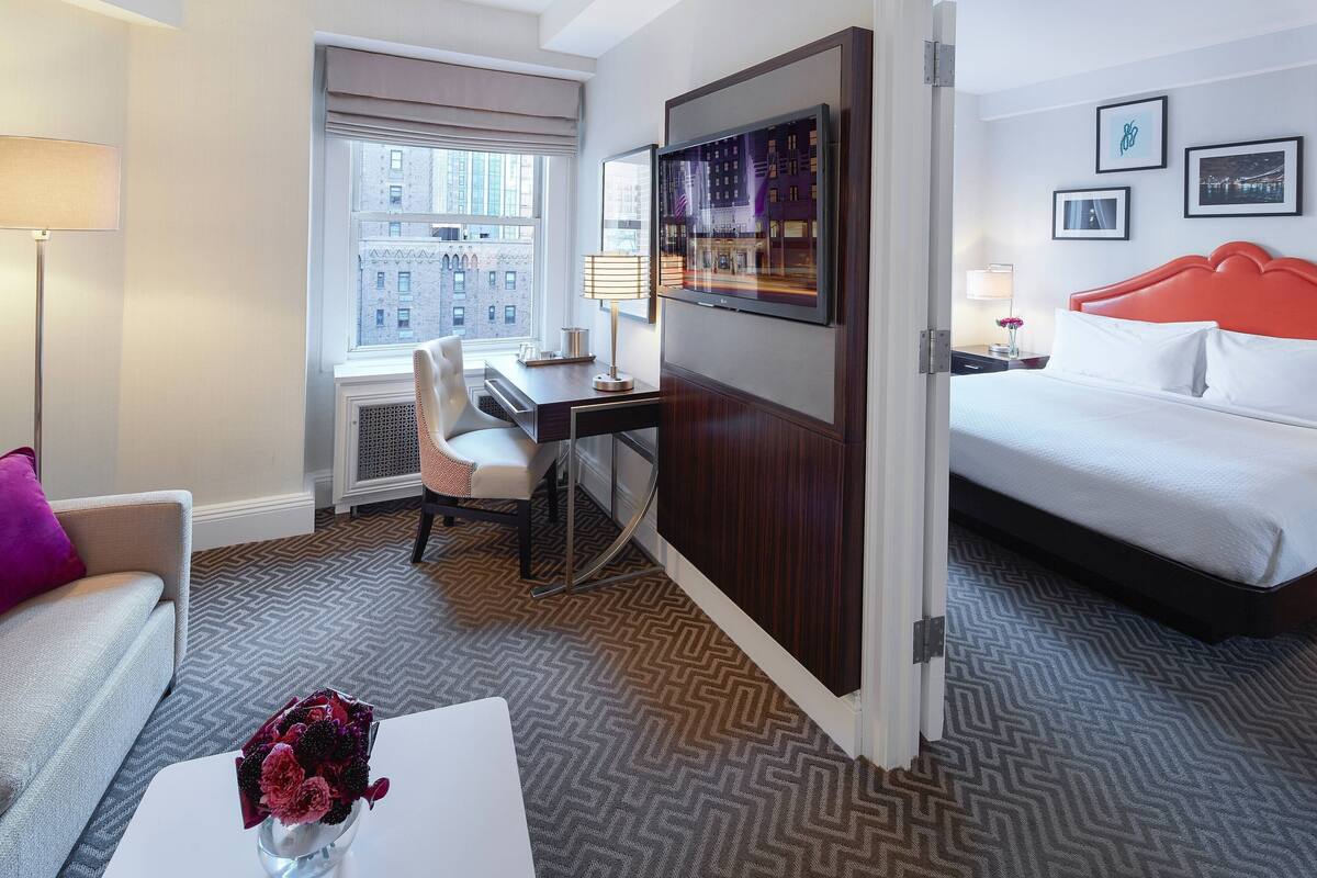 A hotel room with a bed, a desk, a chair, a coffee table, and a window with a city view.